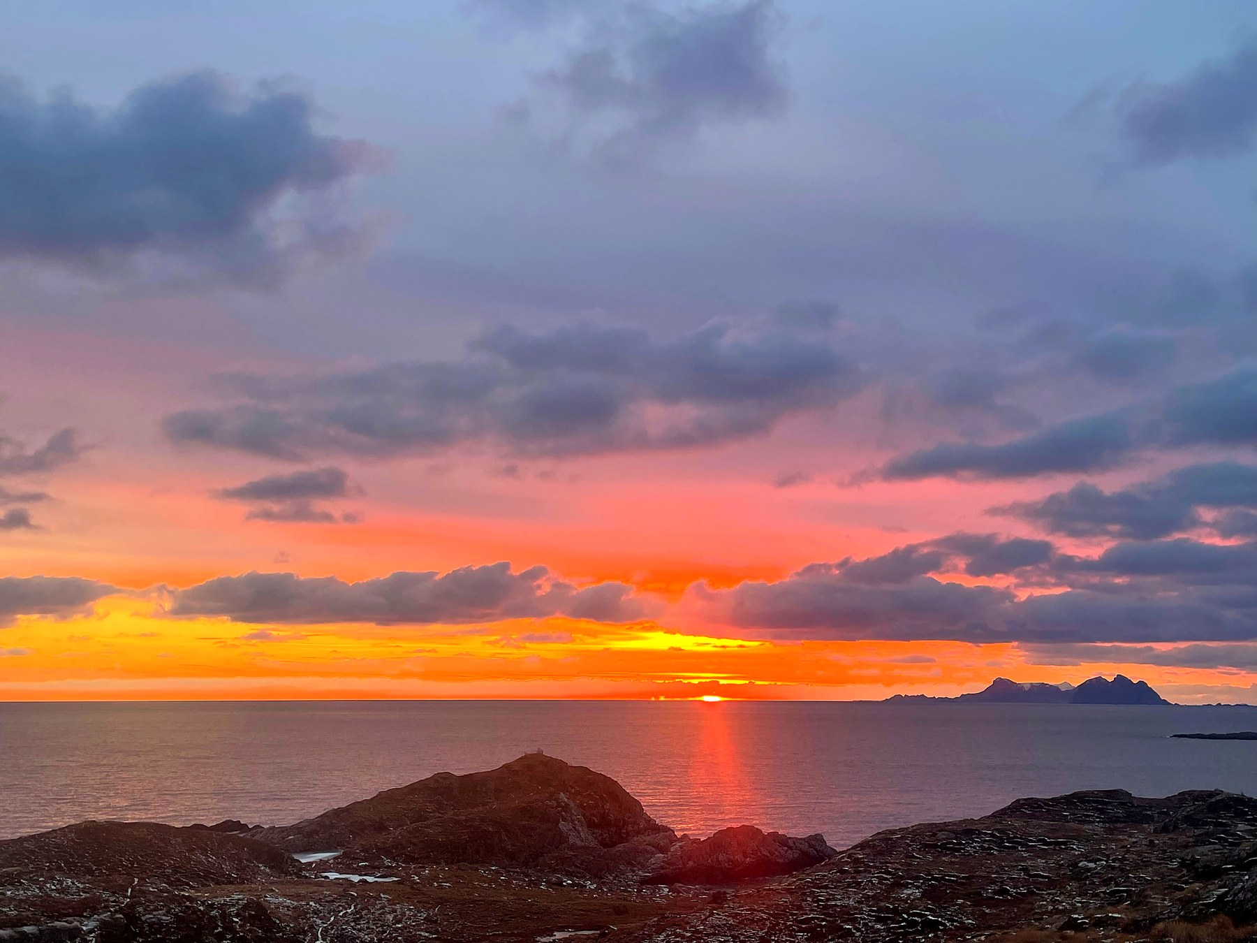 Solnedgang over havet i Lofoten, dramatisk oransje og rosa himmel