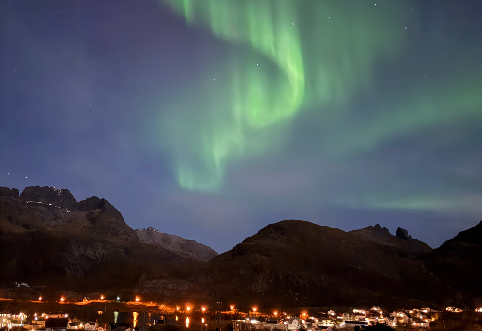 Nordlyset danser over fjellene og hyttene en oktobernatt