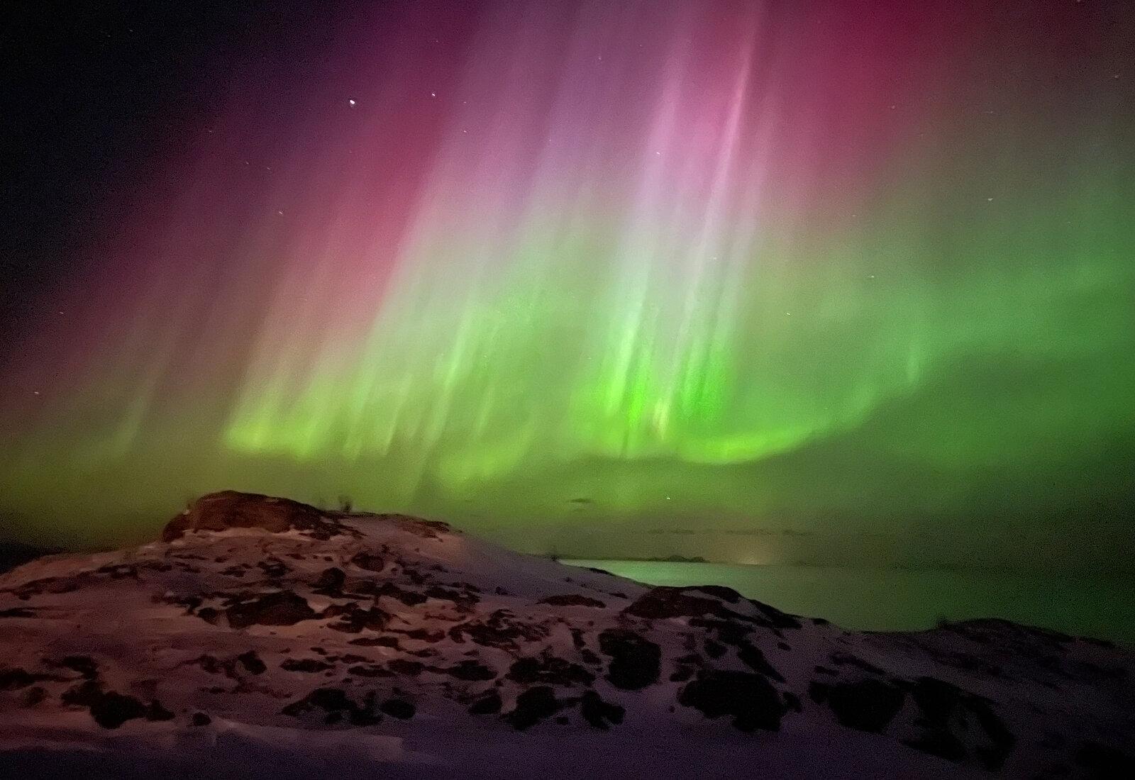 Grønt og rosa nordlys danser over snødekte fjell