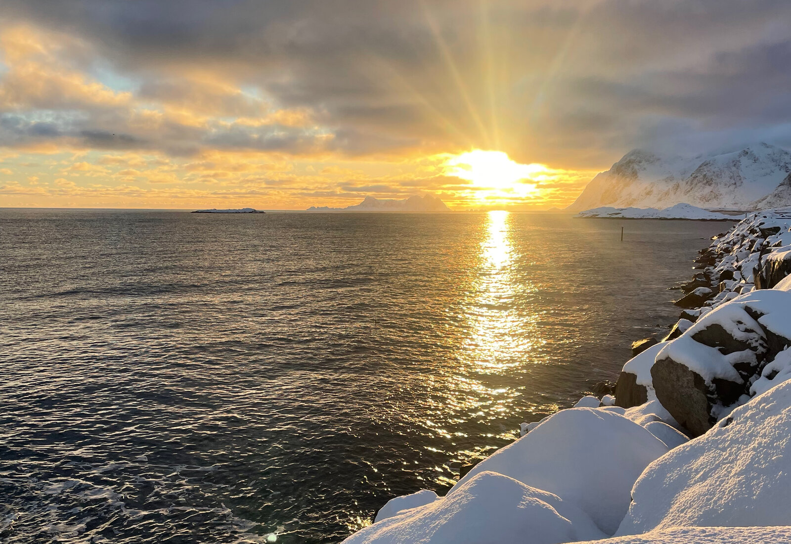 Solstråler over snødekket kystlinje i stillhet